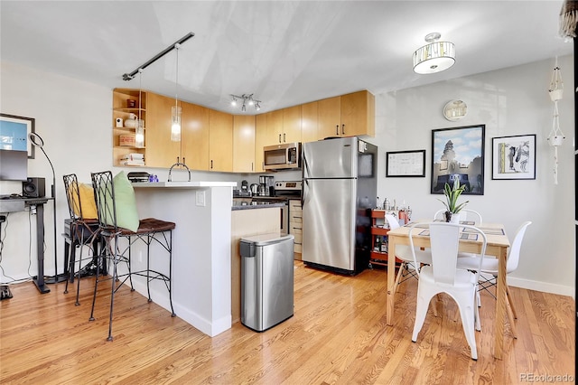 kitchen featuring rail lighting, appliances with stainless steel finishes, decorative light fixtures, kitchen peninsula, and light brown cabinets