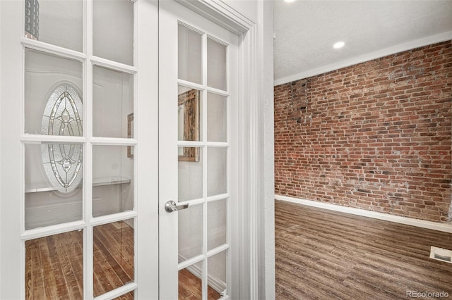 detailed view of brick wall, baseboards, wood finished floors, french doors, and a textured ceiling