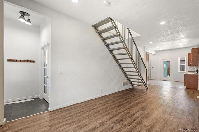 unfurnished living room with stairway, wood finished floors, a sink, baseboards, and recessed lighting