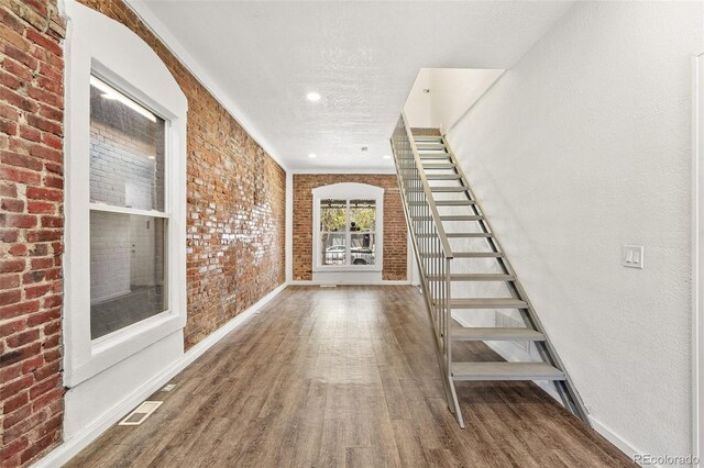 stairs featuring wood finished floors, brick wall, baseboards, recessed lighting, and a textured ceiling