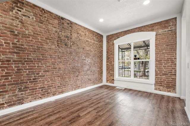 unfurnished room with baseboards, wood finished floors, brick wall, recessed lighting, and a textured ceiling