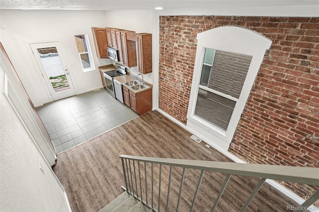 kitchen with appliances with stainless steel finishes, a sink, brick wall, light countertops, and brown cabinetry