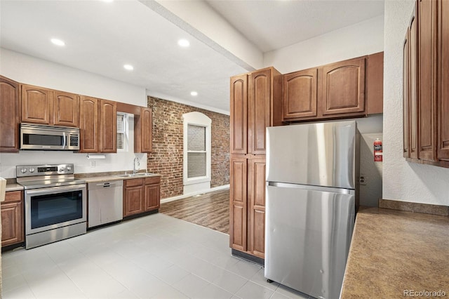 kitchen with stainless steel appliances, a sink, recessed lighting, brown cabinets, and baseboards