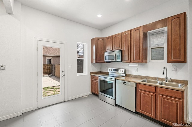 kitchen with stainless steel appliances, a sink, brown cabinetry, light tile patterned floors, and baseboards