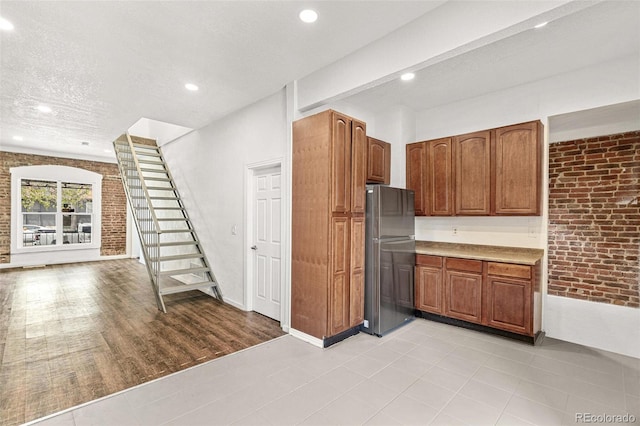 kitchen with freestanding refrigerator, brick wall, recessed lighting, brown cabinets, and light countertops