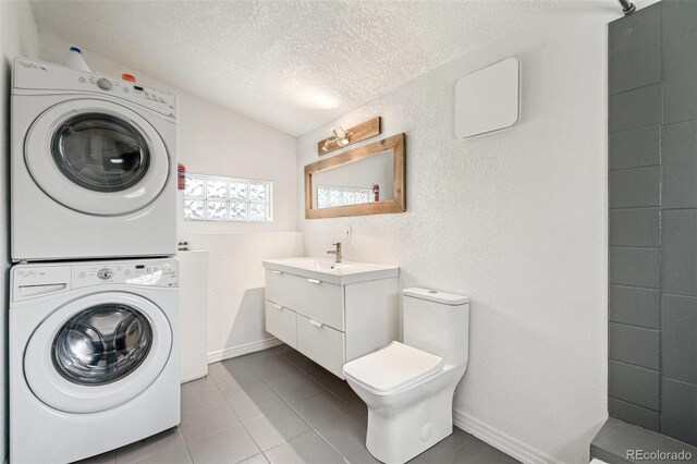 clothes washing area featuring stacked washer / dryer, a textured ceiling, baseboards, and tile patterned flooring