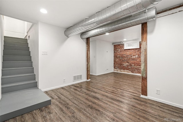 finished below grade area with baseboards, wood finished floors, stairway, brick wall, and recessed lighting