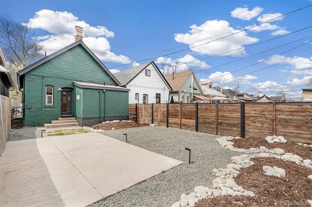 view of front of property with a fenced backyard, a chimney, a patio area, and brick siding