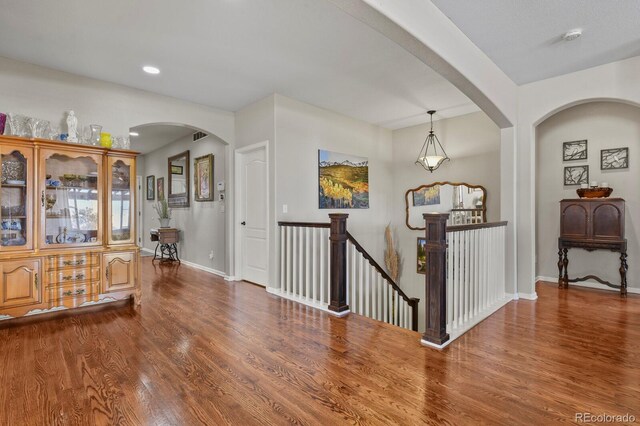 hall with wood finished floors, an upstairs landing, baseboards, and arched walkways