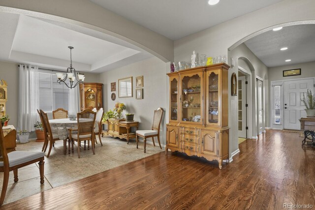 dining space with baseboards, arched walkways, a raised ceiling, and wood finished floors