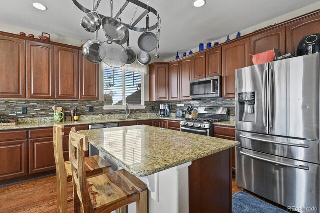 kitchen featuring a breakfast bar, a sink, appliances with stainless steel finishes, decorative backsplash, and light stone countertops