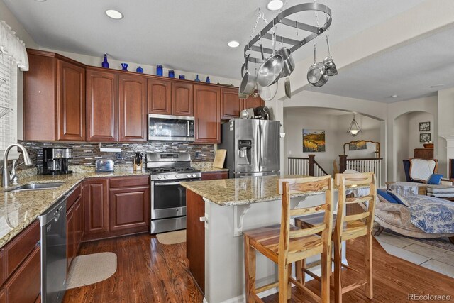 kitchen featuring a breakfast bar, a sink, backsplash, dark wood finished floors, and appliances with stainless steel finishes