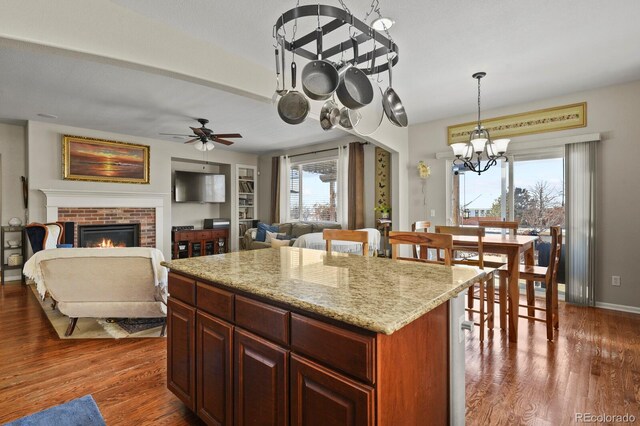 kitchen with hanging light fixtures, a fireplace, a kitchen island, and wood finished floors