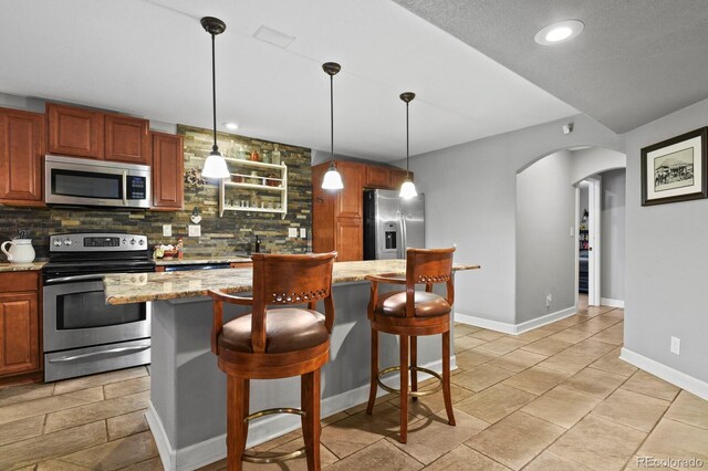 kitchen featuring a kitchen bar, decorative light fixtures, tasteful backsplash, stainless steel appliances, and arched walkways