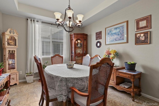 dining room featuring a tray ceiling, a notable chandelier, and baseboards