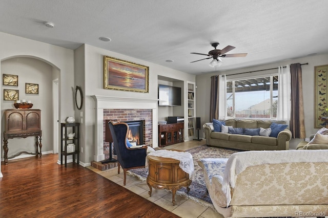 living room with built in features, a fireplace, tile patterned floors, a textured ceiling, and a ceiling fan