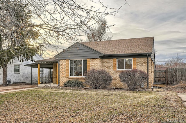 view of front of property with brick siding, a shingled roof, fence, a carport, and a front yard