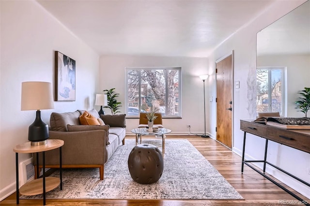 living area featuring light wood-style floors, visible vents, baseboards, and a wealth of natural light