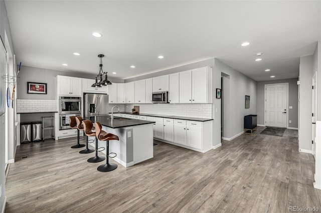 9406 Bross St, Arvada, CO 80007 - kitchen featuring stainless steel appliances, dark countertops, backsplash, a breakfast bar, and light wood-style flooring