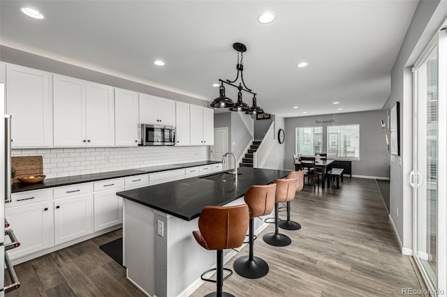 9406 Bross St, Arvada, CO 80007 - kitchen featuring stainless steel microwave, a breakfast bar, dark countertops, tasteful backsplash, and white cabinets