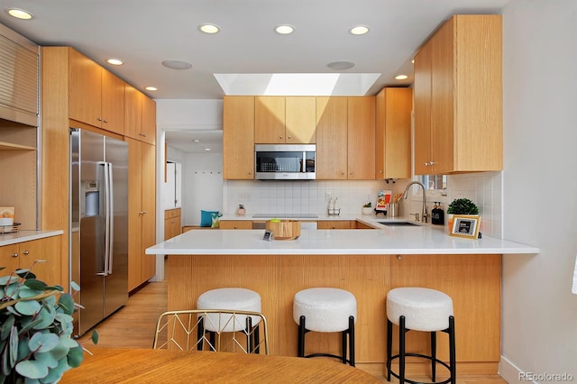 2500 Locust St, Denver, CO 80207 - kitchen featuring appliances with stainless steel finishes, a sink, light wood-style flooring, a skylight, and a peninsula