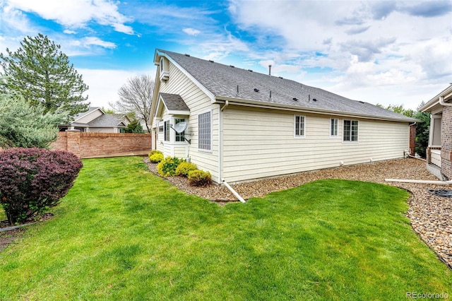 rear view of property featuring a yard, roof with shingles, and fence