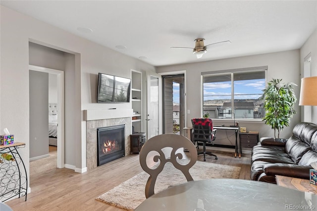 living room with a tile fireplace, ceiling fan, and light hardwood / wood-style floors