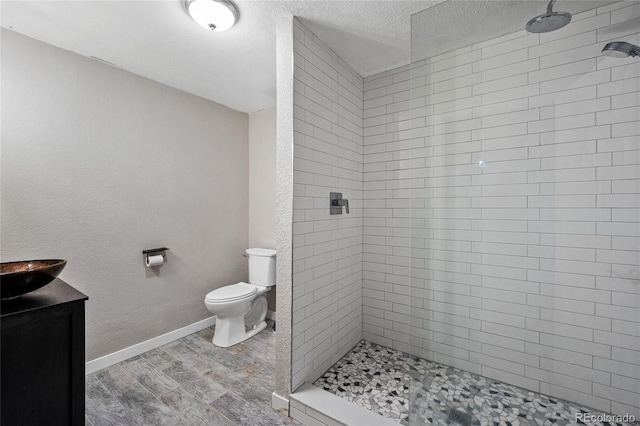 bathroom featuring hardwood / wood-style floors, a tile shower, vanity, a textured ceiling, and toilet