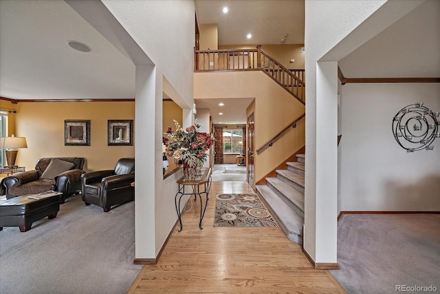 foyer entrance with ornamental molding, light carpet, baseboards, stairway, and light wood-type flooring