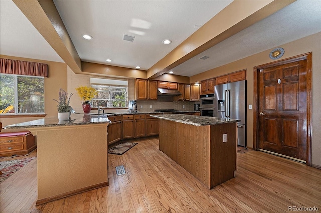 kitchen with a peninsula, appliances with stainless steel finishes, light wood-type flooring, and dark stone counters