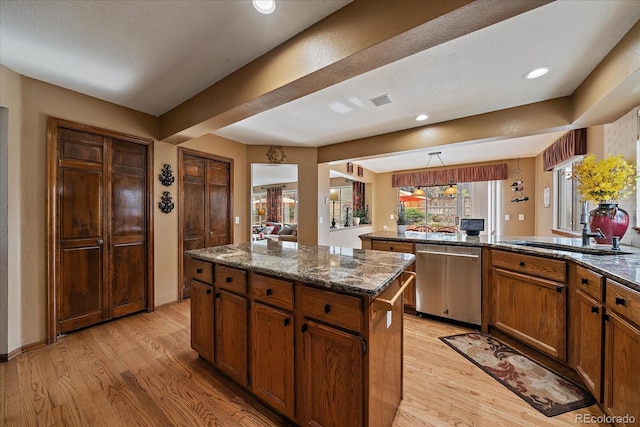 kitchen with a kitchen island, stainless steel dishwasher, light wood-type flooring, a sink, and dark stone countertops