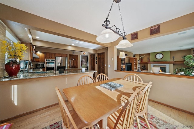 dining area with baseboards, light wood finished floors, and a tile fireplace