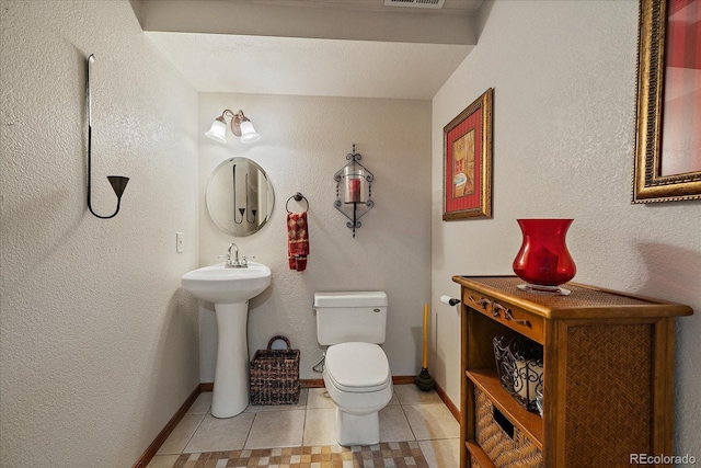 half bath featuring a sink, toilet, tile patterned floors, baseboards, and visible vents