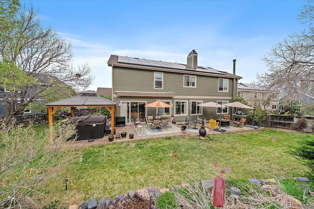 rear view of house featuring solar panels, a lawn, a patio area, a hot tub, and a gazebo