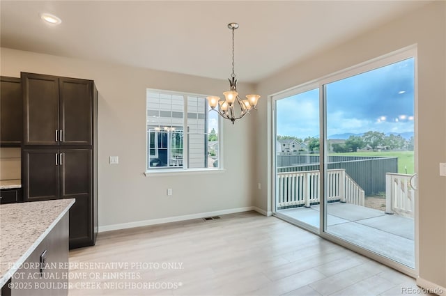 unfurnished dining area with light wood-style flooring, baseboards, and an inviting chandelier