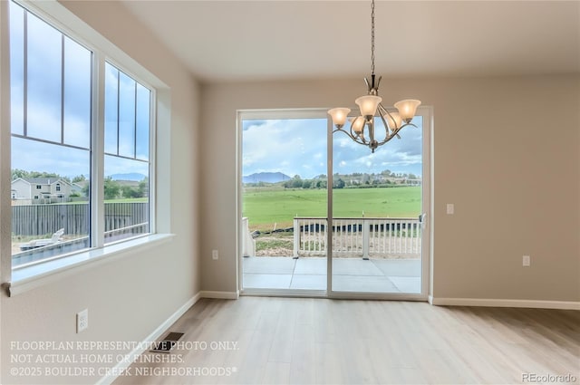 doorway with a notable chandelier, baseboards, a wealth of natural light, and wood finished floors