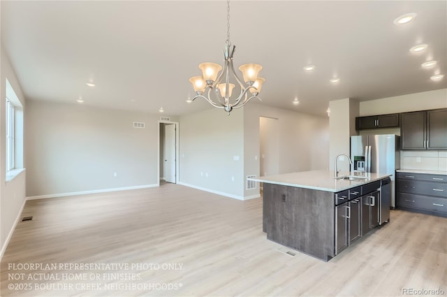 kitchen featuring light wood-style flooring, a sink, visible vents, an island with sink, and decorative light fixtures