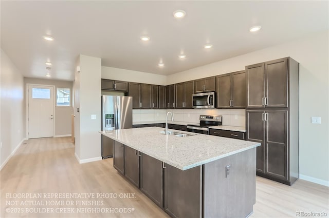 kitchen featuring light stone counters, a sink, dark brown cabinets, appliances with stainless steel finishes, and tasteful backsplash