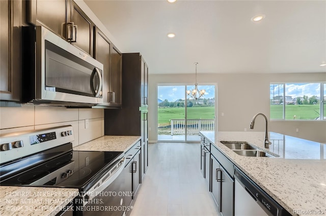 kitchen featuring tasteful backsplash, light stone counters, appliances with stainless steel finishes, dark brown cabinets, and a sink