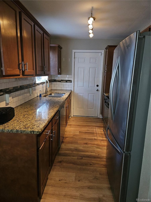 kitchen featuring sink, appliances with stainless steel finishes, light stone countertops, light hardwood / wood-style floors, and decorative backsplash