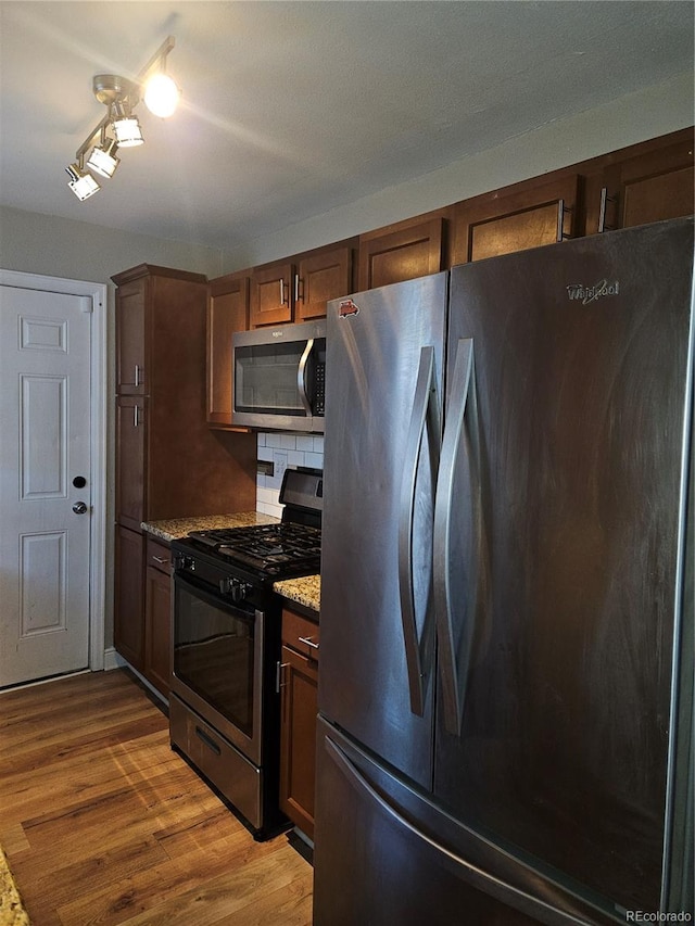 kitchen with decorative backsplash, light stone countertops, light hardwood / wood-style floors, and appliances with stainless steel finishes