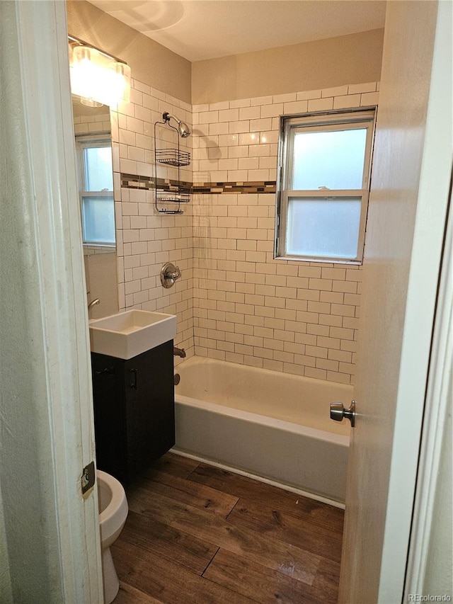 full bathroom with wood-type flooring, tiled shower / bath combo, vanity, and toilet