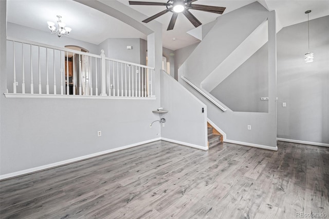 unfurnished living room featuring a ceiling fan, wood finished floors, baseboards, and a chandelier