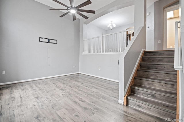 staircase featuring ceiling fan, a chandelier, wood finished floors, baseboards, and lofted ceiling