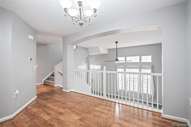 spare room with arched walkways, a chandelier, wood finished floors, a ceiling fan, and baseboards