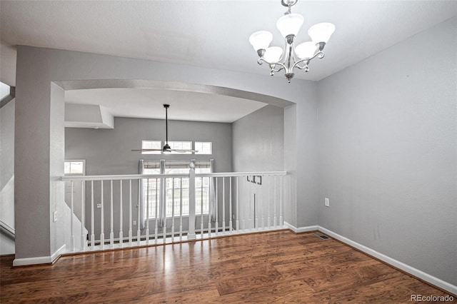 spare room featuring a chandelier, ceiling fan, baseboards, wood finished floors, and arched walkways
