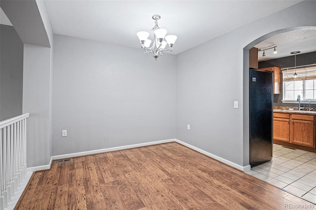 unfurnished dining area with arched walkways, rail lighting, a sink, a chandelier, and light wood-type flooring
