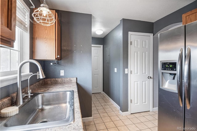 kitchen with stainless steel fridge, a sink, light tile patterned floors, brown cabinetry, and baseboards