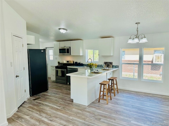 kitchen with hanging light fixtures, white cabinetry, kitchen peninsula, black appliances, and light hardwood / wood-style flooring