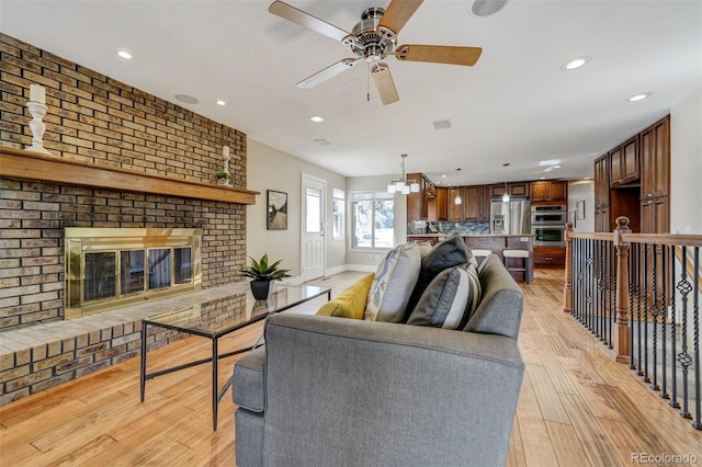 living room featuring a fireplace, ceiling fan, and light wood-type flooring